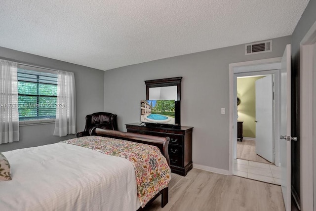 bedroom with baseboards, a textured ceiling, visible vents, and light wood-style floors