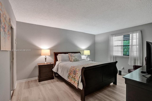 bedroom with baseboards, a textured ceiling, and light wood-type flooring