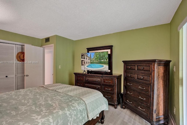bedroom with a closet, a textured ceiling, visible vents, and light wood-type flooring
