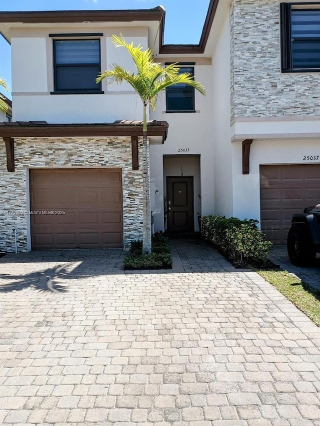 view of property with stucco siding, a garage, stone siding, and decorative driveway