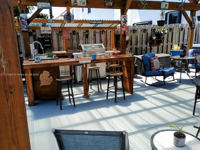 wooden terrace with outdoor dry bar, area for grilling, and fence