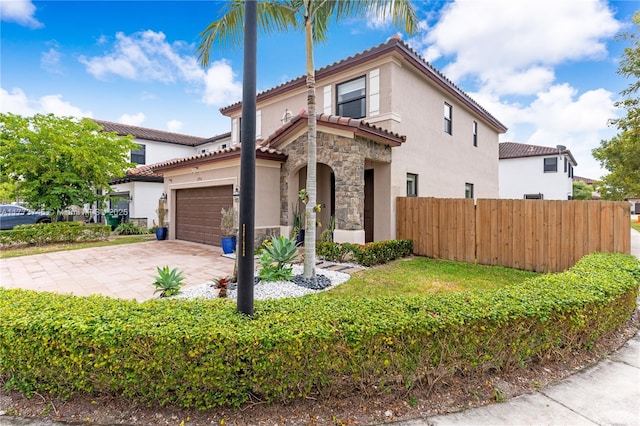 mediterranean / spanish home with driveway, stone siding, stucco siding, fence, and a tiled roof