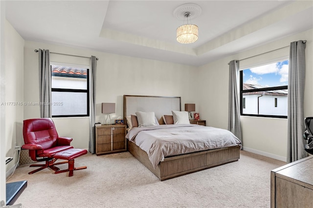 carpeted bedroom with baseboards, a tray ceiling, and multiple windows