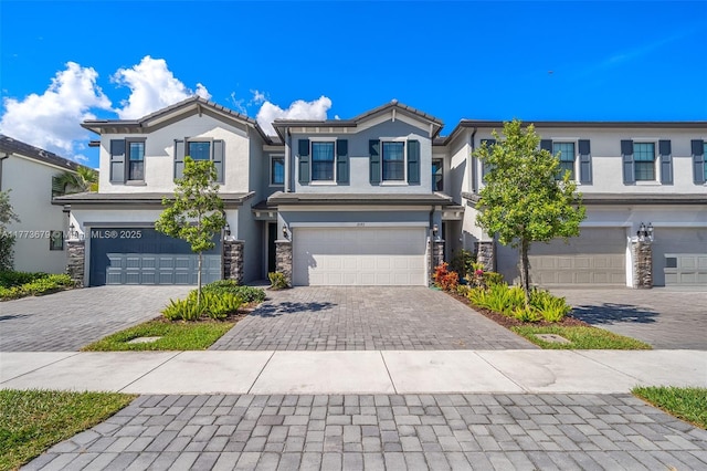 view of front facade featuring decorative driveway, stucco siding, a garage, and stone siding