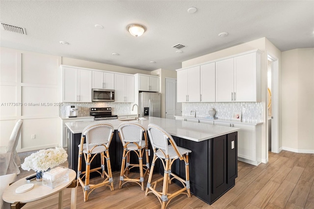 kitchen with light countertops, appliances with stainless steel finishes, an island with sink, and visible vents