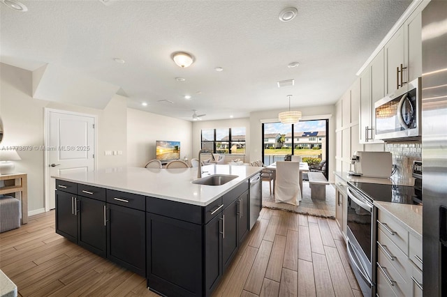 kitchen with open floor plan, a center island with sink, a sink, and appliances with stainless steel finishes