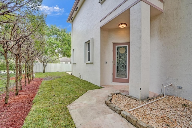 entrance to property featuring a lawn, stucco siding, and fence