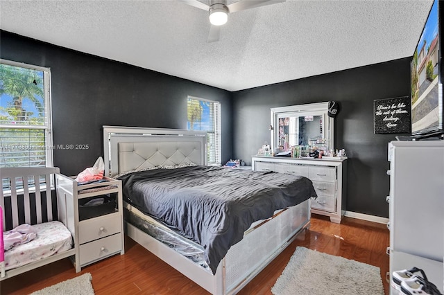 bedroom featuring multiple windows, wood finished floors, baseboards, and a textured ceiling
