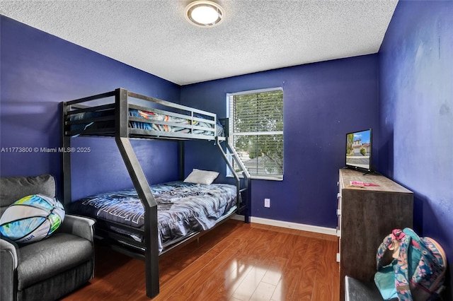 bedroom with a textured ceiling, baseboards, and wood finished floors