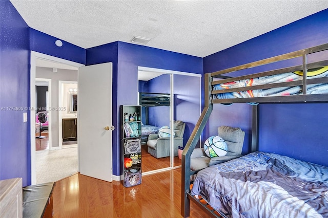bedroom with visible vents, a textured ceiling, a closet, and wood finished floors