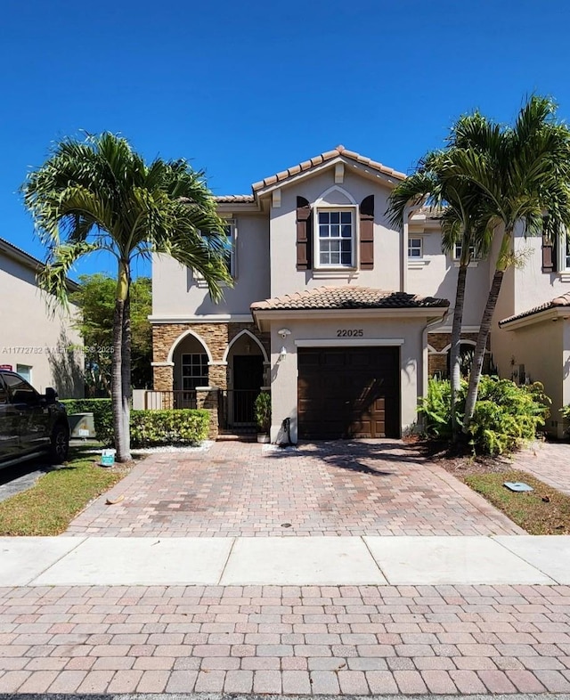 mediterranean / spanish-style house featuring a tiled roof, decorative driveway, stucco siding, and an attached garage