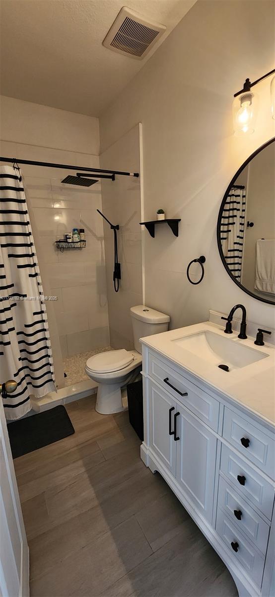 full bathroom featuring toilet, tiled shower, vanity, wood finished floors, and visible vents