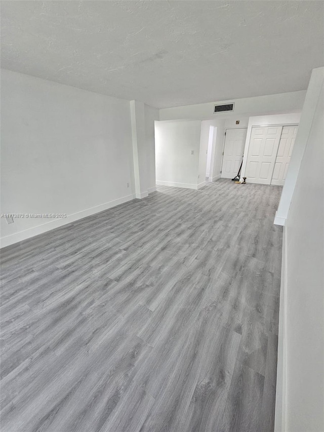 unfurnished living room featuring visible vents, baseboards, a textured ceiling, and wood finished floors