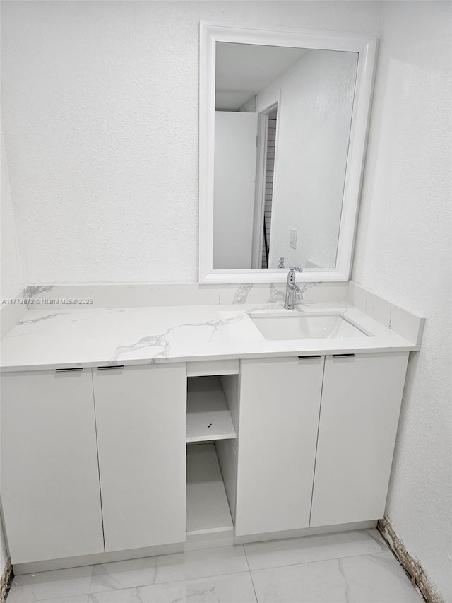 bathroom featuring marble finish floor, a textured wall, and vanity