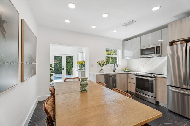kitchen featuring modern cabinets, stainless steel appliances, a sink, french doors, and backsplash