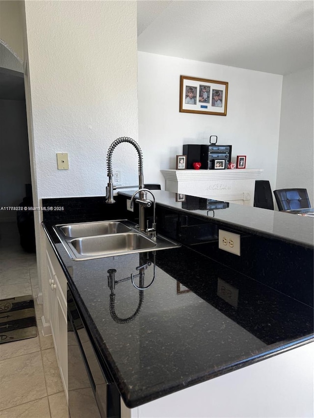 kitchen with a sink, dark stone counters, dishwasher, white cabinetry, and light tile patterned floors