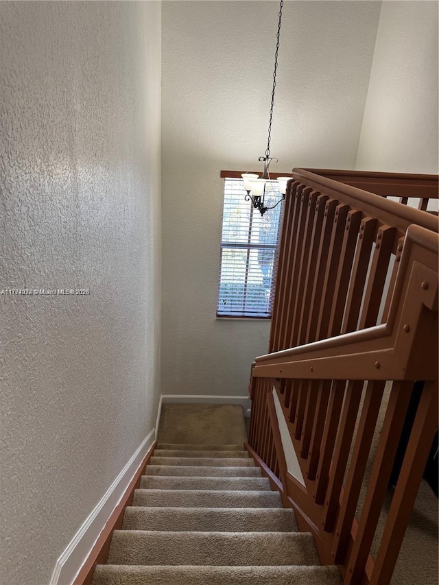 stairs featuring a chandelier, a textured wall, baseboards, and carpet floors