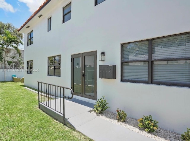 entrance to property featuring fence, a lawn, a tile roof, stucco siding, and french doors