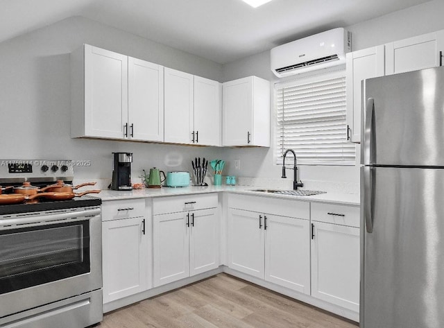 kitchen featuring a sink, white cabinetry, a wall unit AC, light wood-type flooring, and stainless steel appliances