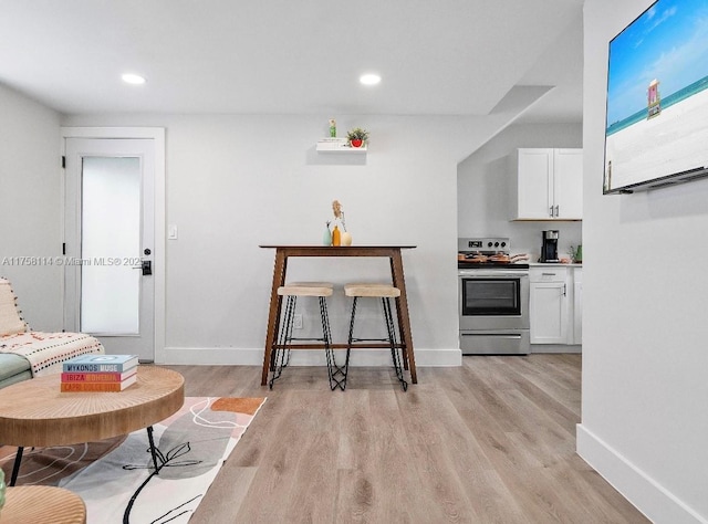 kitchen with baseboards, stainless steel range with electric cooktop, white cabinets, and light wood-type flooring