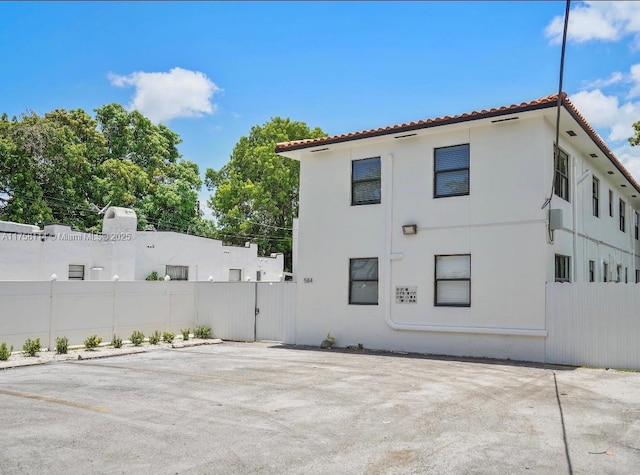 rear view of property featuring stucco siding, a tile roof, and fence