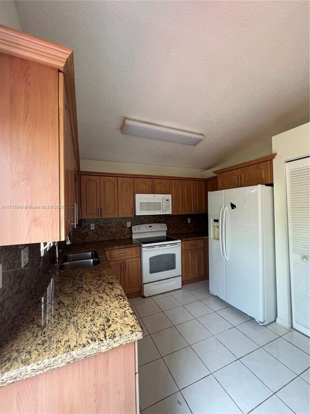 kitchen featuring tasteful backsplash, white appliances, a sink, light tile patterned flooring, and brown cabinets