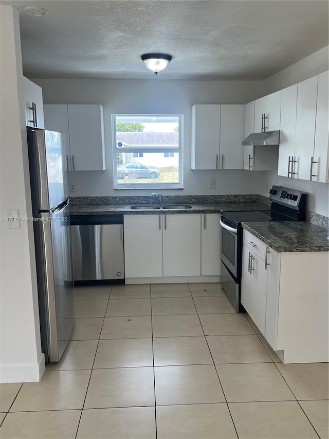 kitchen featuring white cabinetry, light tile patterned floors, under cabinet range hood, a sink, and appliances with stainless steel finishes