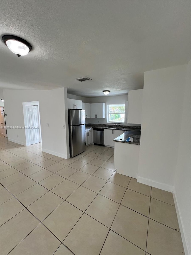 kitchen with light tile patterned flooring, visible vents, stainless steel appliances, dark countertops, and white cabinetry