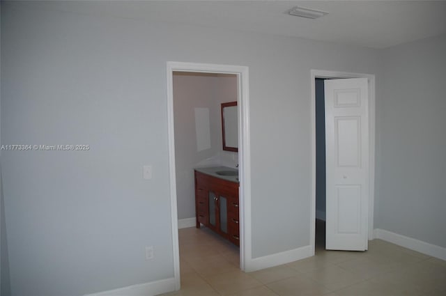 unfurnished bedroom featuring light tile patterned flooring, baseboards, connected bathroom, and a sink