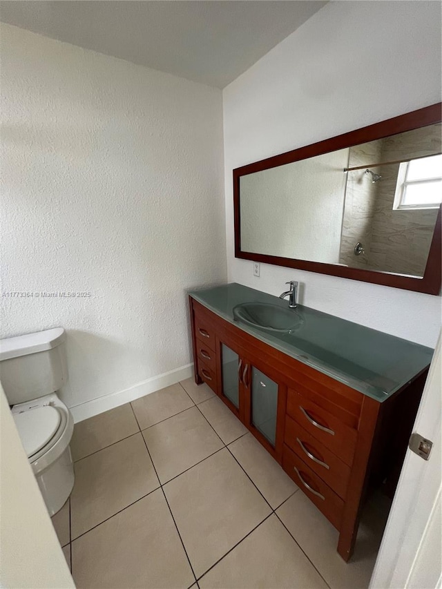 full bathroom with vanity, a tile shower, toilet, baseboards, and tile patterned floors