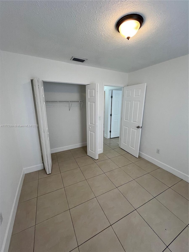 unfurnished bedroom with baseboards, a closet, a textured ceiling, and visible vents