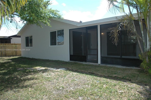 rear view of house featuring a sunroom, stucco siding, fence, and a lawn