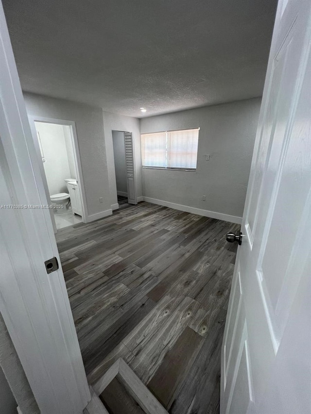 unfurnished bedroom featuring baseboards, a textured ceiling, wood finished floors, and connected bathroom