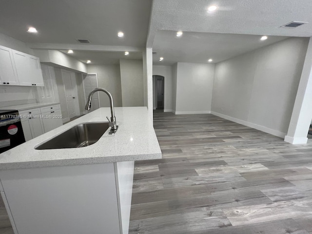 kitchen with a sink, light wood-type flooring, baseboards, visible vents, and white cabinets