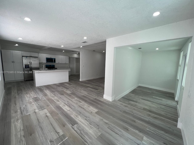 kitchen featuring baseboards, open floor plan, light wood-style flooring, and stainless steel refrigerator with ice dispenser