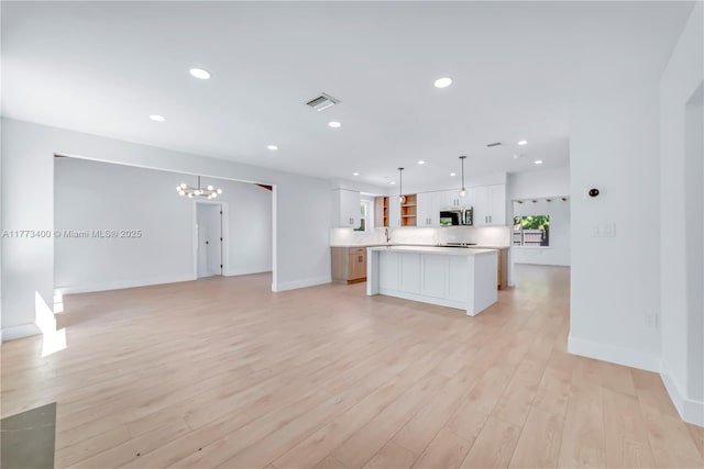 kitchen with stainless steel microwave, light wood-style floors, a chandelier, and visible vents