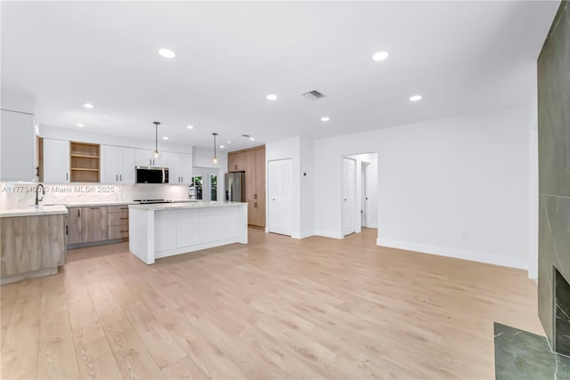 kitchen with light countertops, open shelves, light wood-type flooring, stainless steel appliances, and visible vents