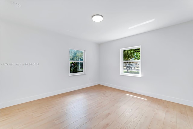 unfurnished room featuring baseboards, light wood finished floors, and plenty of natural light