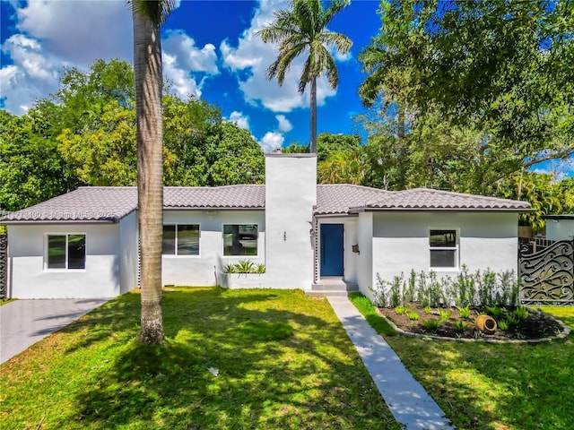 mediterranean / spanish house with a tile roof, a front yard, stucco siding, and a chimney
