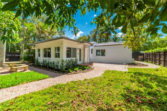 back of property featuring a tiled roof, stucco siding, fence, and a lawn