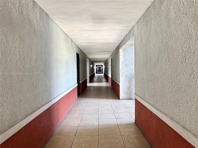 hall with light tile patterned flooring and a textured wall