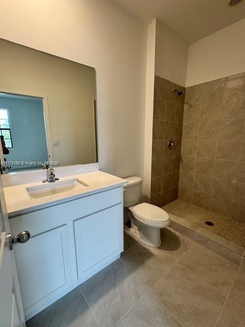 bathroom with toilet, vanity, tile patterned flooring, and tiled shower