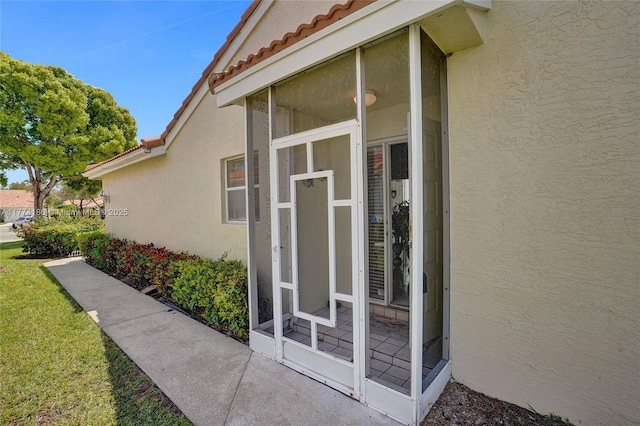 doorway to property featuring stucco siding, a lawn, and a tile roof