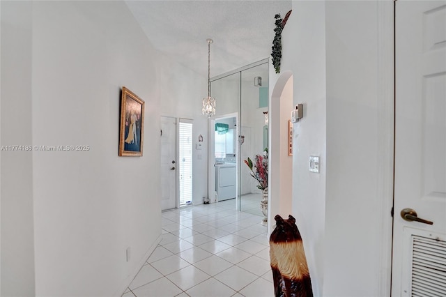hall featuring washer / clothes dryer, baseboards, light tile patterned floors, arched walkways, and a towering ceiling