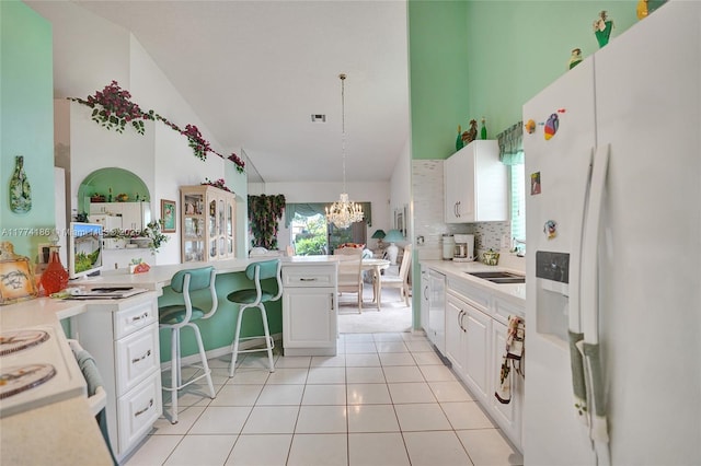 kitchen with white fridge with ice dispenser, a chandelier, white cabinetry, high vaulted ceiling, and a sink