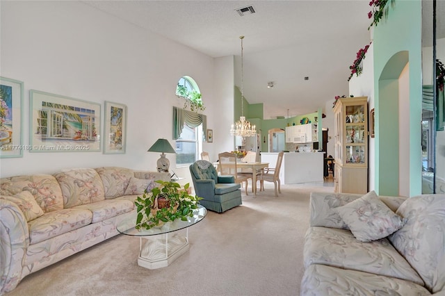 carpeted living area featuring high vaulted ceiling, an inviting chandelier, and visible vents