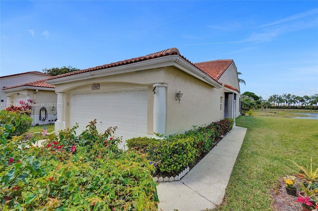 view of side of property featuring a tiled roof, an attached garage, a lawn, and stucco siding