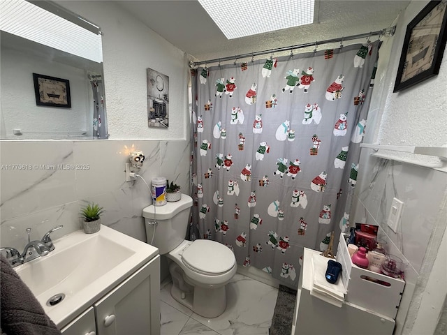 bathroom with toilet, vanity, curtained shower, marble finish floor, and a textured wall