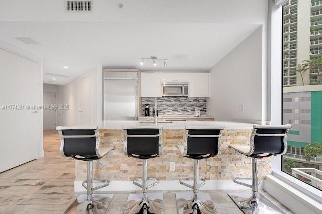 1300 Brickell Bay Dr Unit 601, Miami, FL 33131 - kitchen with visible vents, light wood-type flooring, a breakfast bar, stainless steel appliances, and white cabinetry
