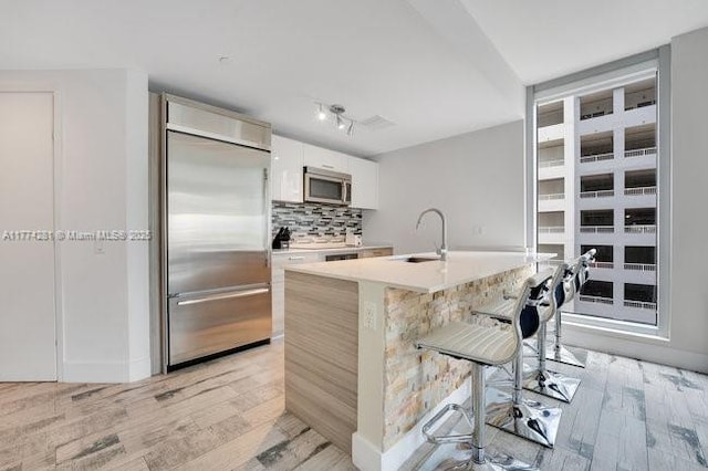 1300 Brickell Bay Dr Unit 601, Miami, FL 33131 - kitchen with a kitchen breakfast bar, appliances with stainless steel finishes, tasteful backsplash, a sink, and light wood-style flooring